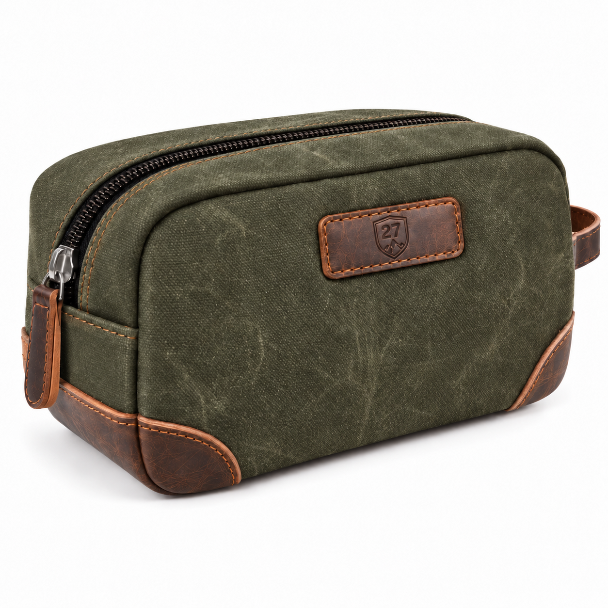 An olive green canvas toiletry bag with brown leather trim and a black zipper, featuring a brown leather patch with an embossed shield logo on the front.
